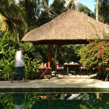 Thatched-roof pool villa at Amandari with stone platform, framed by tropical vegetation and clear sky.