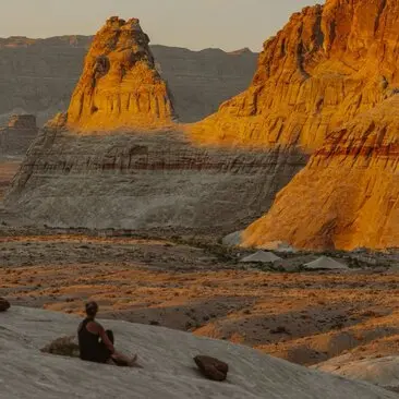 Yoga session on red rock formations at Amangiri at sunrise, with a guest seated on the desert floor facing towering sandstone cliffs.