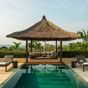 Amanjiwo's thatched pool pavilion overlooks a rectangular plunge pool with surrounding loungers and verdant landscape.