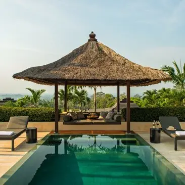Thatched pavilion overlooking plunge pool at Amanjiwo resort, Indonesia, with Borobudur temple visible on distant hillside.