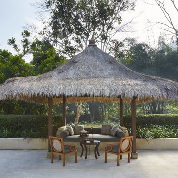 Garden pavilion with thatched roof at Amanjiwo, featuring wooden seating beneath.