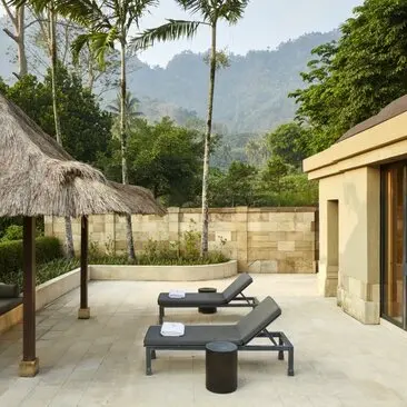 Pavilion taman di Amanjiwo dengan tempat tidur matahari dan atap jerami tradisional menghadap pegunungan.