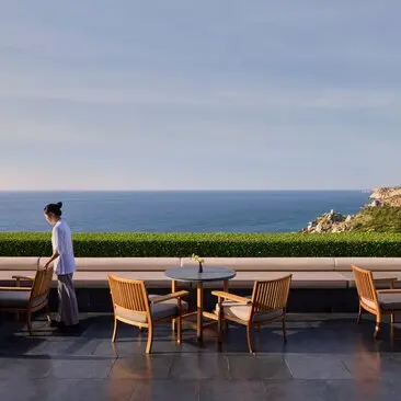 Amanoi's main restaurant terrace overlooking the sea, with wooden dining tables and a solitary figure gazing at the coastline.