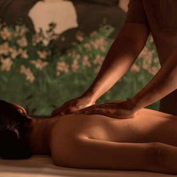 Therapist performing a massage treatment in a spa room at Amanoi, Vietnam, with warm lighting and green botanical elements.