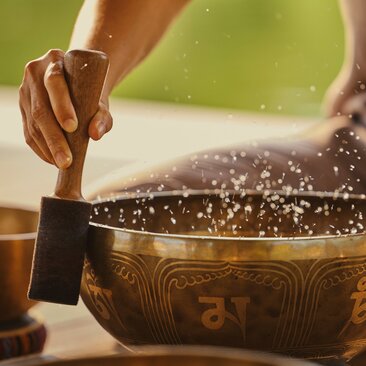 Hands striking a singing bowl during sound healing meditation at Amanoi spa and wellness centre.