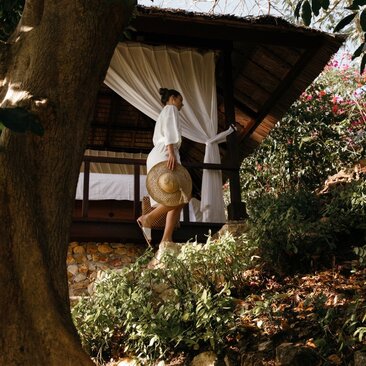 Outdoor spa pavilion at Amanpulo resort in the Philippines, with a therapist preparing a treatment space beneath a wooden structure draped in white fabric.