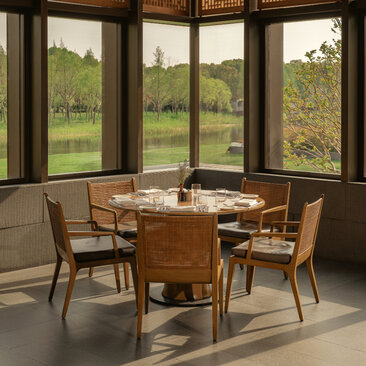 Dining area at Amanyangyun with round wooden table, mid-century chairs, and floor-to-ceiling windows overlooking green landscape.