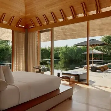 Principal bedroom at Amanyara with floor-to-ceiling windows overlooking tropical grounds and wooden ceiling beams.