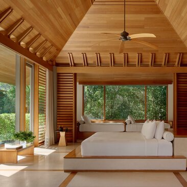 Spacious bedroom at Amanyara with wooden ceiling, large windows overlooking tropical gardens, and a central bed.