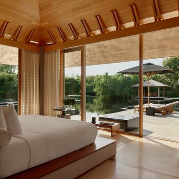 Principal bedroom at Amanyara with wooden ceiling beams, cream furnishings, and expansive views towards the terrace and landscape beyond.