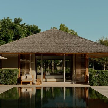 Amanyara villa pavilion with thatched roof reflected in still pool, surrounded by tropical vegetation.