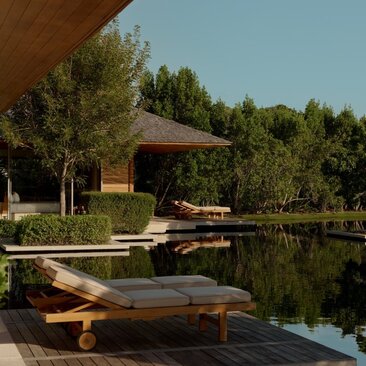 Wooden lounger on a deck overlooking a tranquil pond at Amanyara, with a pavilion and trees beyond.