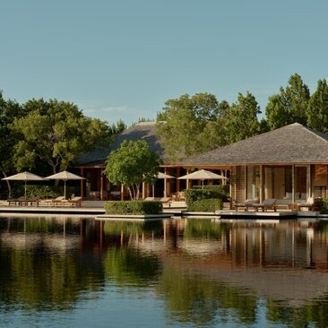 Tranquility Pond at Amanyara, reflecting wooden pavilions and lush vegetation under clear sky.