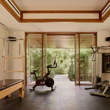 Gym at Amanyara with wooden-framed glass doors opening to garden views, exercise equipment and natural light.