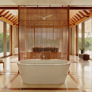 Freestanding bathtub in Amanyara bathroom with wooden slat accent wall and natural light from floor-to-ceiling windows.