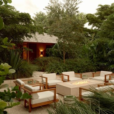 Fire pit and seating area at Amanyara villa, surrounded by tropical vegetation at dusk.