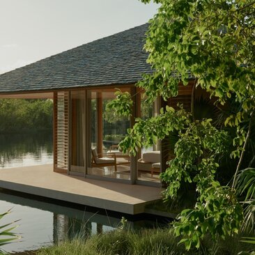 Amanyara villa pavilion with wooden shutters overlooking still water, framed by climbing vines.