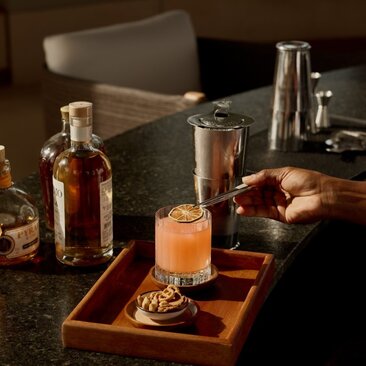Cocktail served on a wooden tray at Amanyara's resort bar, with spirit bottles and bar tools arranged on the counter.