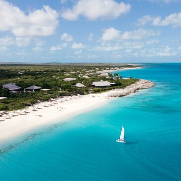 Aerial view of Amanyara's white sand beach and turquoise waters with a sailboat offshore, Turks and Caicos.