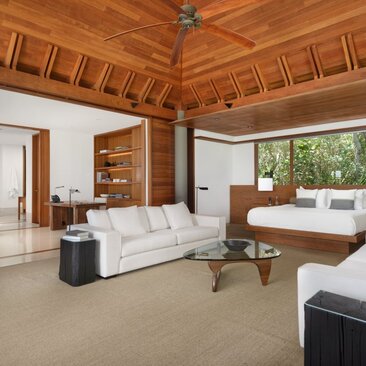 Principal bedroom at Amanyara with warm wooden ceiling, neutral furnishings, and natural light from windows.