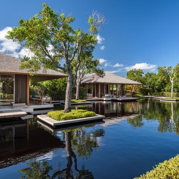 Wooden villa with pond at Amanyara, Turks and Caicos, surrounded by lush vegetation under clear skies.