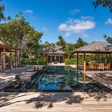 Pool area at Amanyara with thatched pavilions and tropical gardens under clear blue sky.
