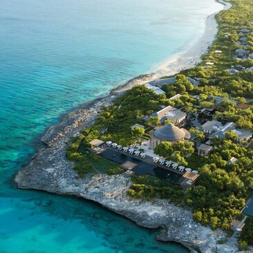 Aerial view of Amanyara resort in Turks and Caicos, with turquoise waters meeting a pristine sandy beach bordered by lush vegetation.