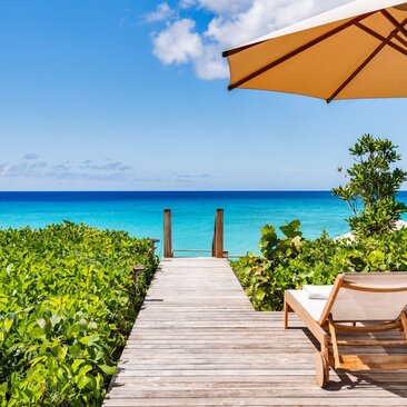 Wooden beach path leading to turquoise waters at Amanyara, with lounger and umbrella in foreground.