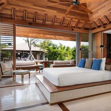 Spacious bedroom at Amanyara with wooden ceiling, platform bed, and open views to tropical garden and sala beyond.