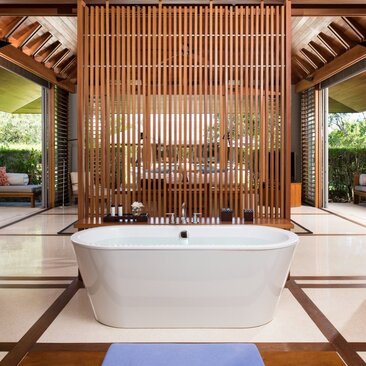 Freestanding white bathtub in a principal bedroom at Amanyara, framed by wooden partition screens and natural light.