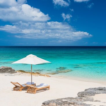 White parasol and wooden lounger on white sand beach with turquoise waters at Amanyara, Turks and Caicos.