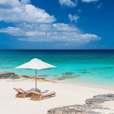 White parasol and wooden lounger on white sand beach overlooking turquoise waters at Amanyara, Turks and Caicos.