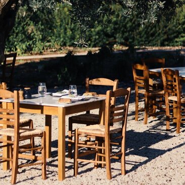 Wooden dining tables and rush-seat chairs arranged in sunlit outdoor courtyard at Amanzoe, Greece.