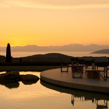 Amanzoe resort at dusk, with silhouetted architecture overlooking calm waters and distant mountains bathed in golden light.