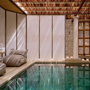 Spa pool at Amanzoe resort in Greece, with natural light filtering through slatted screens beside a daybed.