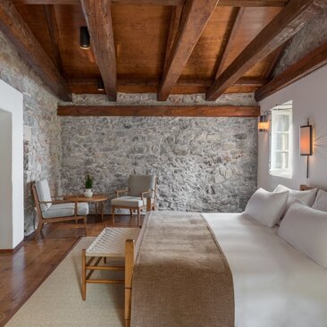 Principal bedroom at Aman Sveti Stefan with exposed wooden beams and stone wall accent.