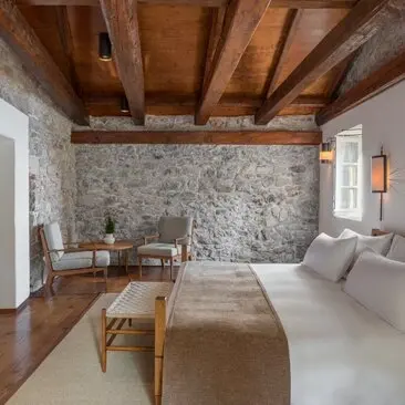 Principal bedroom at Aman Sveti Stefan with exposed wooden beams and stone wall accent.