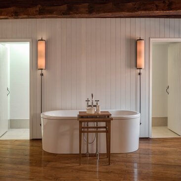 Bathroom at Aman Sveti Stefan with freestanding oval bathtub, wooden flooring, and wall-mounted copper fixtures.