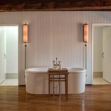 Bathroom at Aman Sveti Stefan with freestanding oval bathtub, wooden flooring, and wall-mounted copper fixtures.