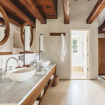 Principal bathroom at Aman Sveti Stefan with marble countertop, wooden beams, and natural light from terrace doors.