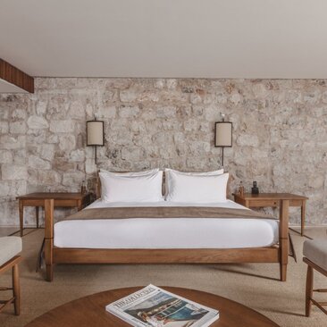 Principal bedroom at Aman Sveti Stefan featuring a wooden bed with white linens and stone accent wall.