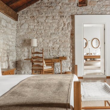 Principal bedroom in a two-bedroom suite at Aman Sveti Stefan, featuring stone walls and wooden furnishings.