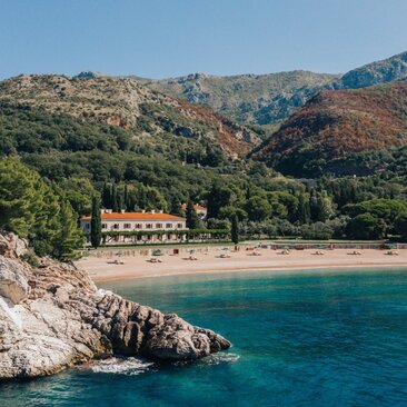 Villa Milocer overlooks the Adriatic Sea at Aman Sveti Stefan, with rocky outcrops and pine-forested hills beyond.