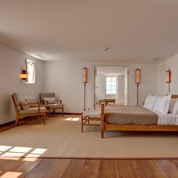 Principal bedroom at Aman Sveti Stefan with wooden bed, chair, and natural light from windows.