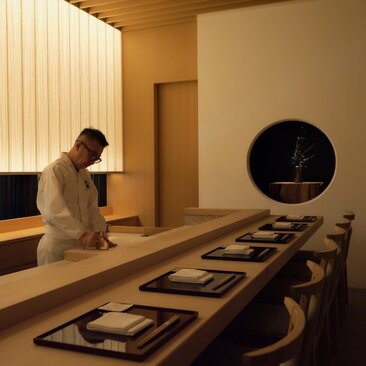 Musashi dining venue at Aman Tokyo, with chef preparing food at counter and place settings arranged along table.