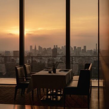 Dining table and chairs silhouetted against floor-to-ceiling windows overlooking Tokyo's skyline at sunset, Aman Tokyo.