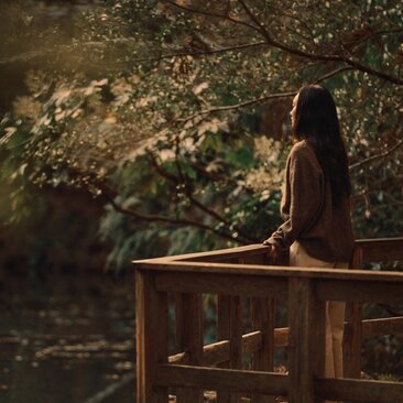 Woman seated on wooden bench beneath dappled forest light at Amanemu, Japan.