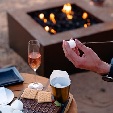 S'mores and fire pit gathering at Amangiri resort, USA, with guests holding drinks by the flames.