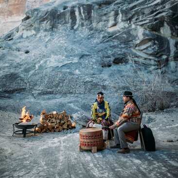Zwei Menschen sitzen bei Sonnenuntergang an einem Lagerfeuer vor einer Felswand im Amangiri Resort.