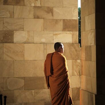 Buddhist monk in saffron robes walking through stone corridor at Amanjiwo resort, Indonesia.